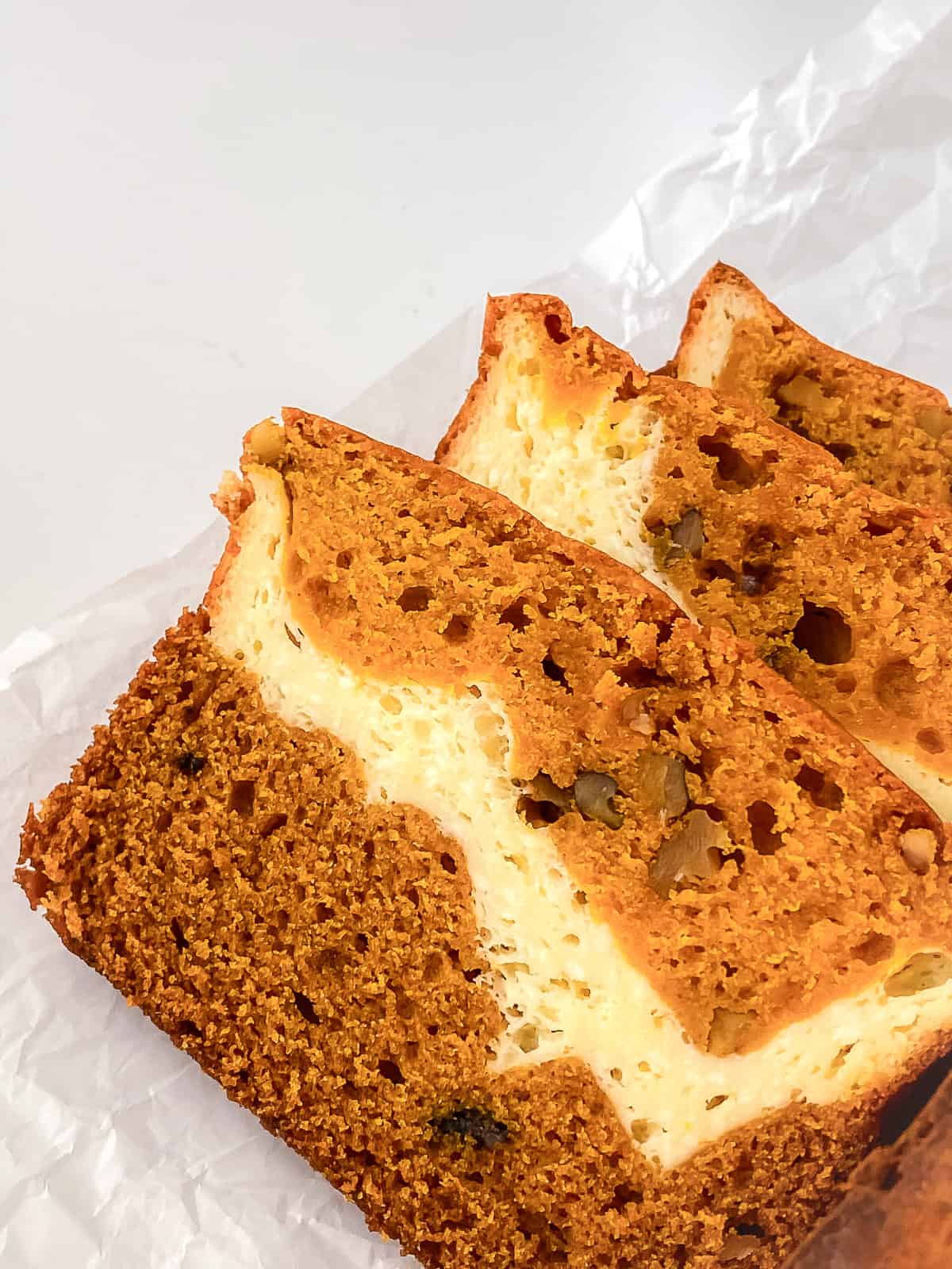 Three slices of cream cheese pumpkin bread laid on parchment paper showing the creamy cheesecake-style layer and moist crumb.