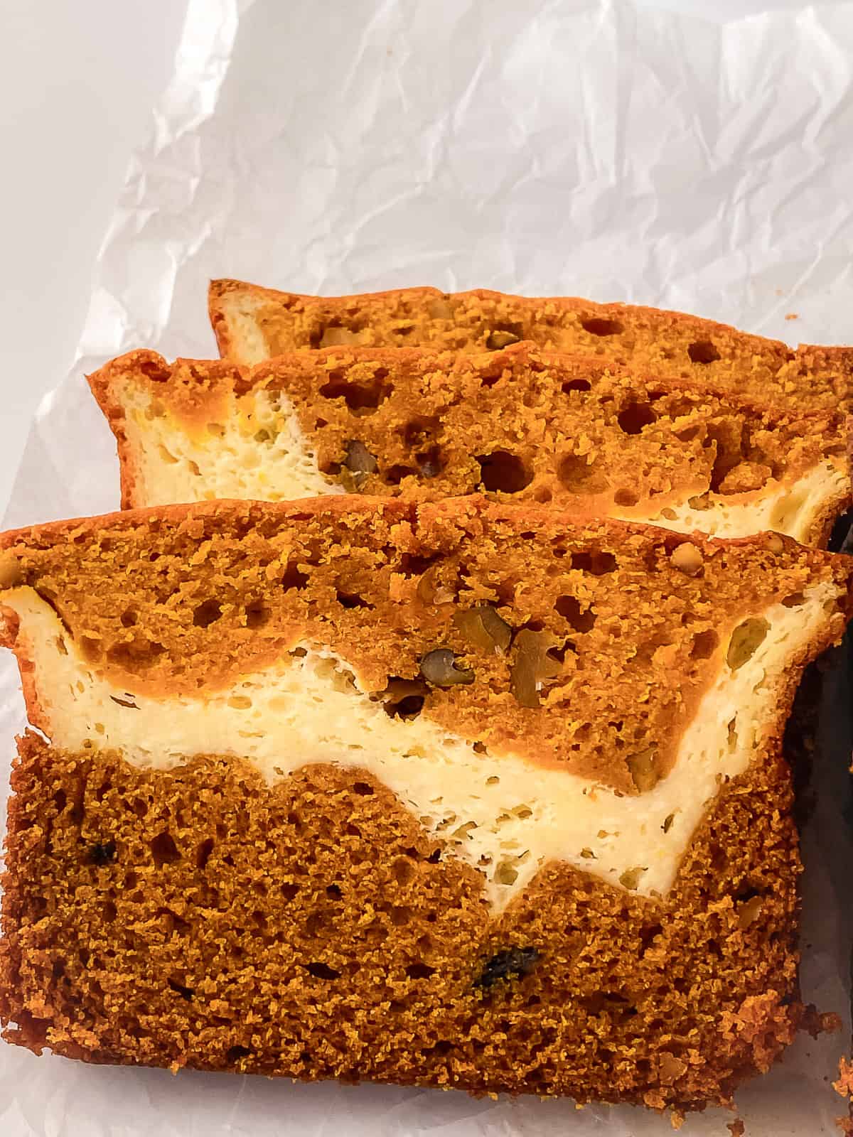 Close-up of sliced cream cheese pumpkin bread highlighting the rich pumpkin color, chopped walnuts, and creamy filling.