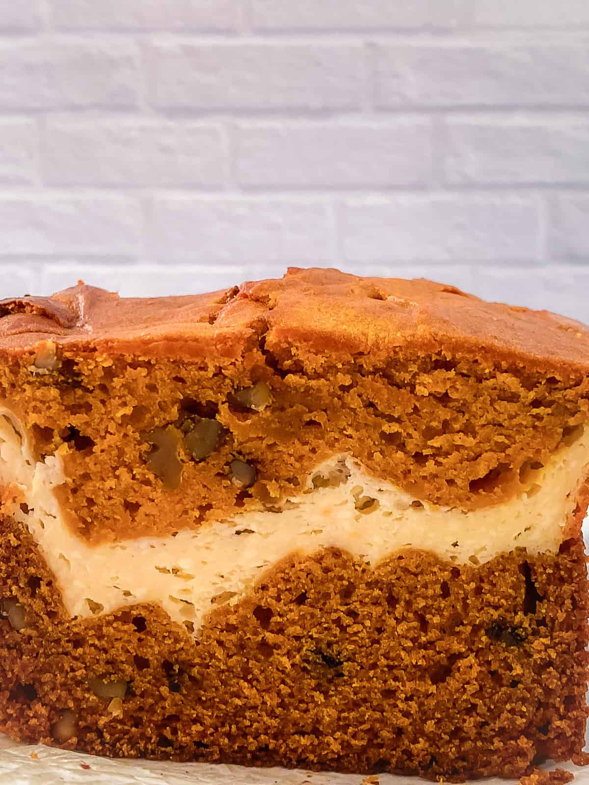 Side view of a thick slice of cream cheese pumpkin bread on parchment paper showing the distinct cream cheese layer.