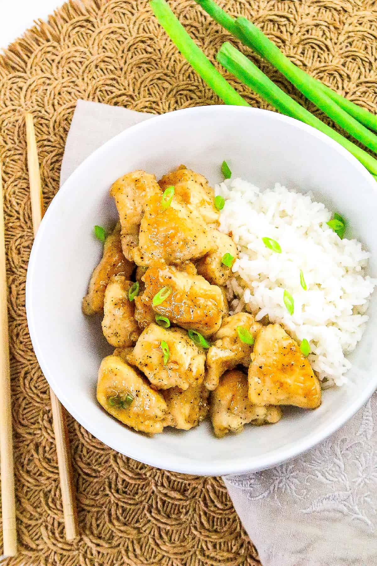 Bowl of honey butter chicken with steamed white rice, garnished with green onions.