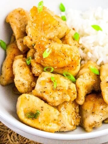 Close-up view of golden honey butter chicken with rice and chopped green onions.