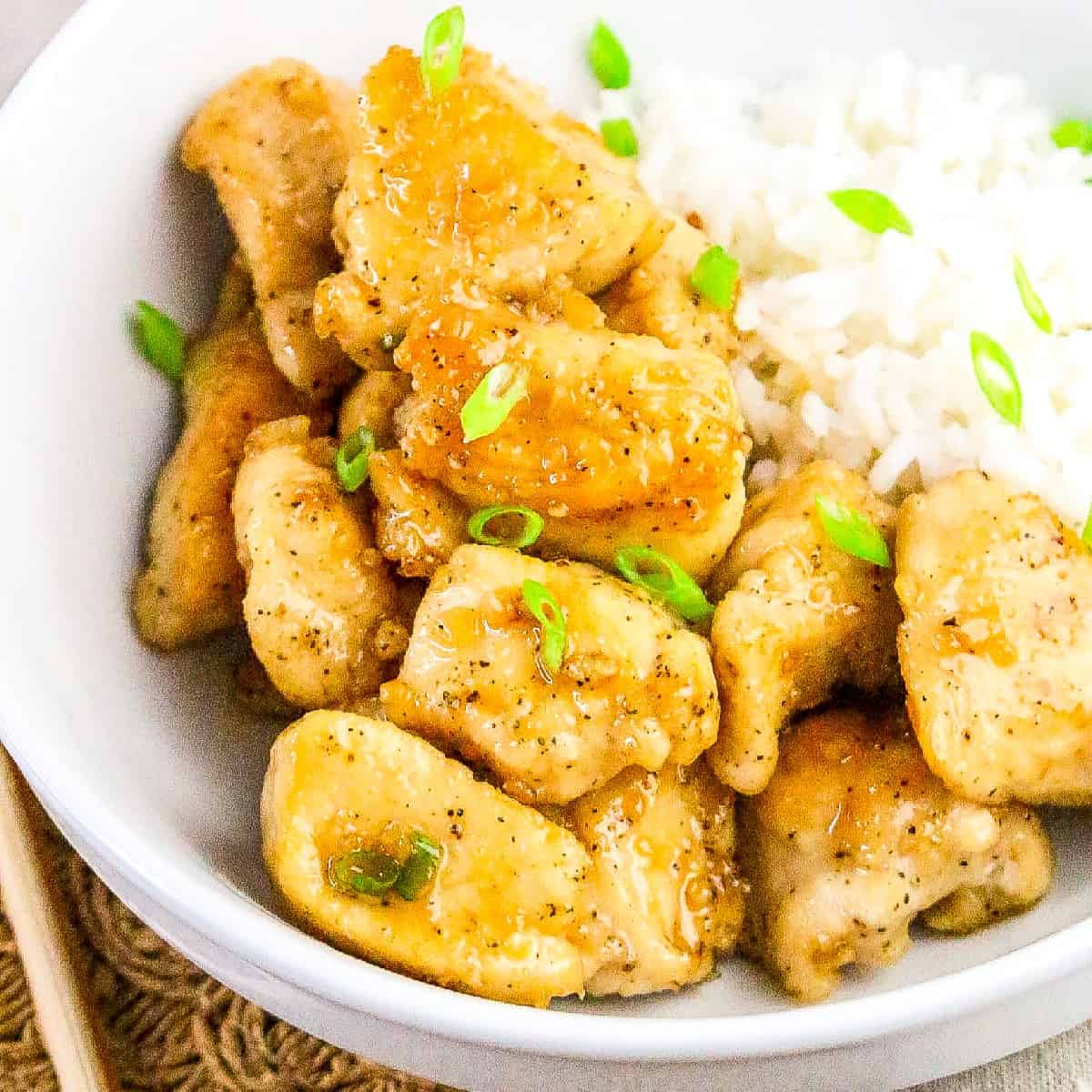 Close-up view of golden honey butter chicken with rice and chopped green onions.