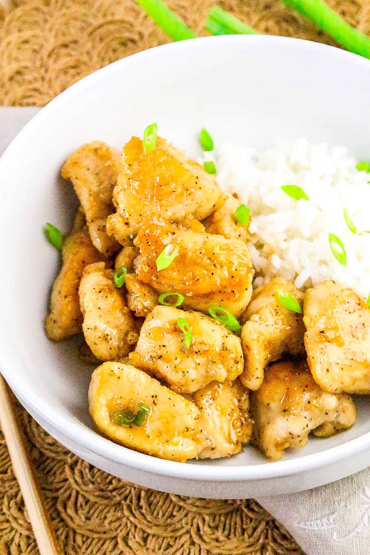 Close-up of golden honey butter chicken with rice and chopped green onions.