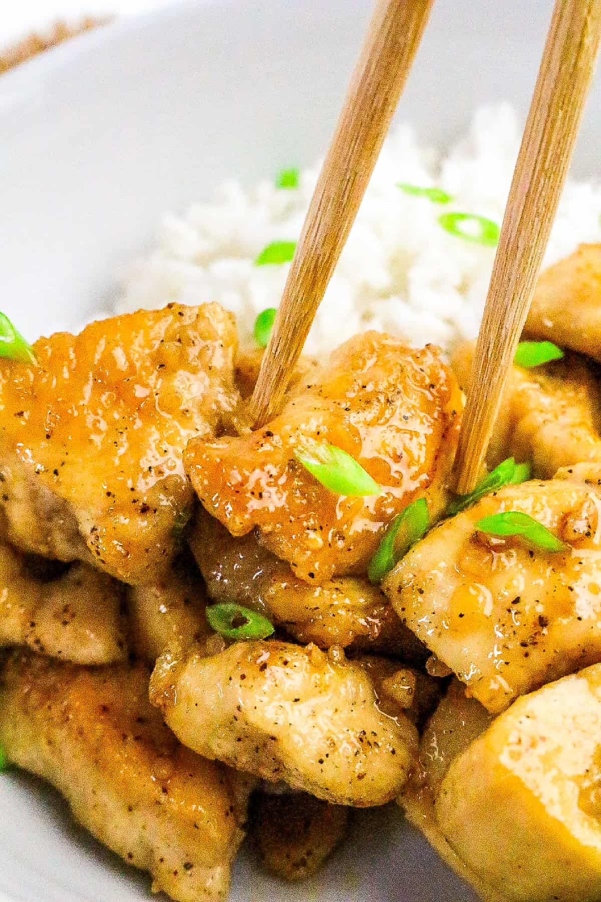 Chopsticks holding a piece of honey butter chicken glazed in garlic honey sauce.