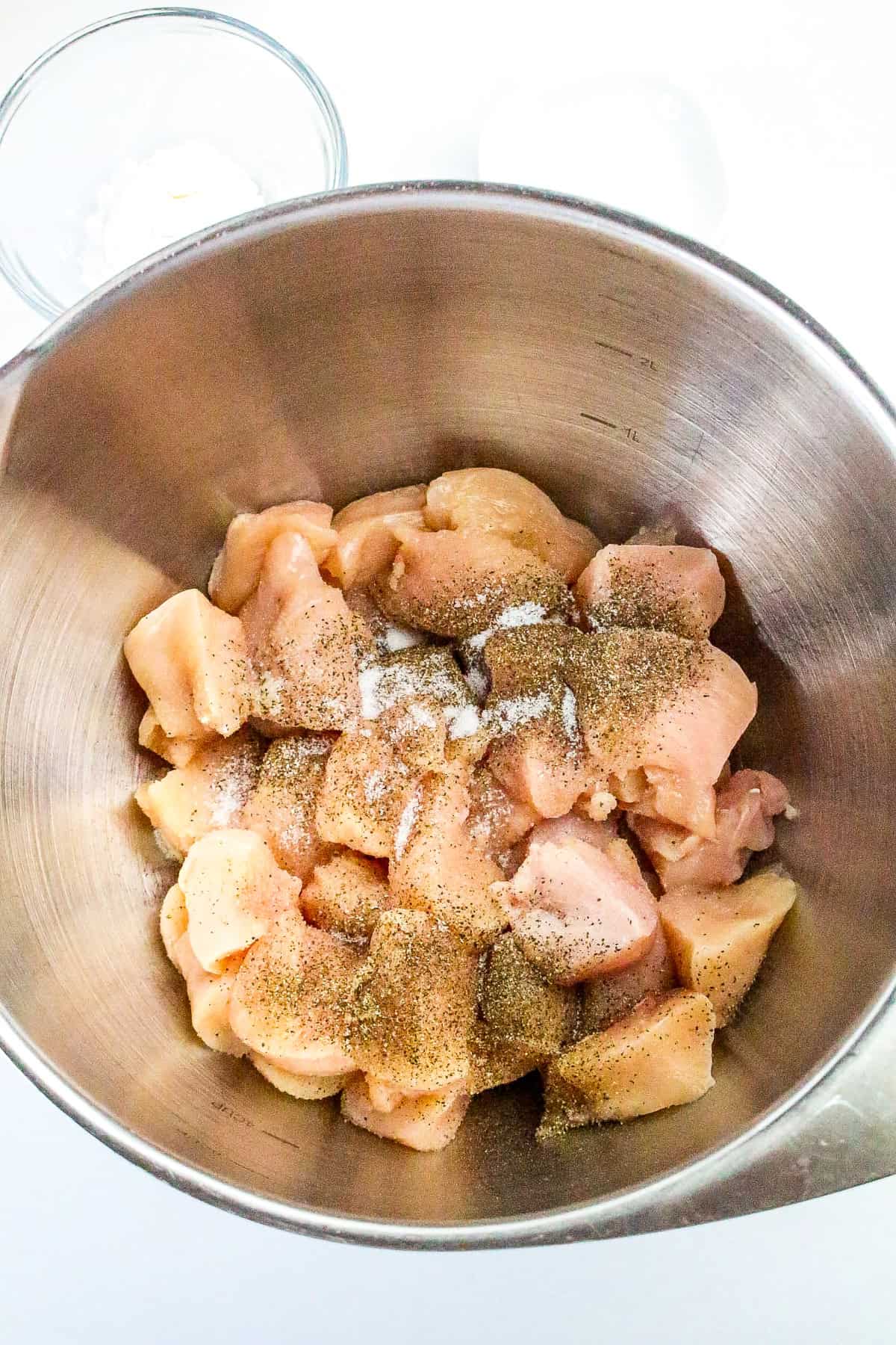 Raw chicken chunks in a mixing bowl seasoned with salt and black pepper for honey butter chicken.
