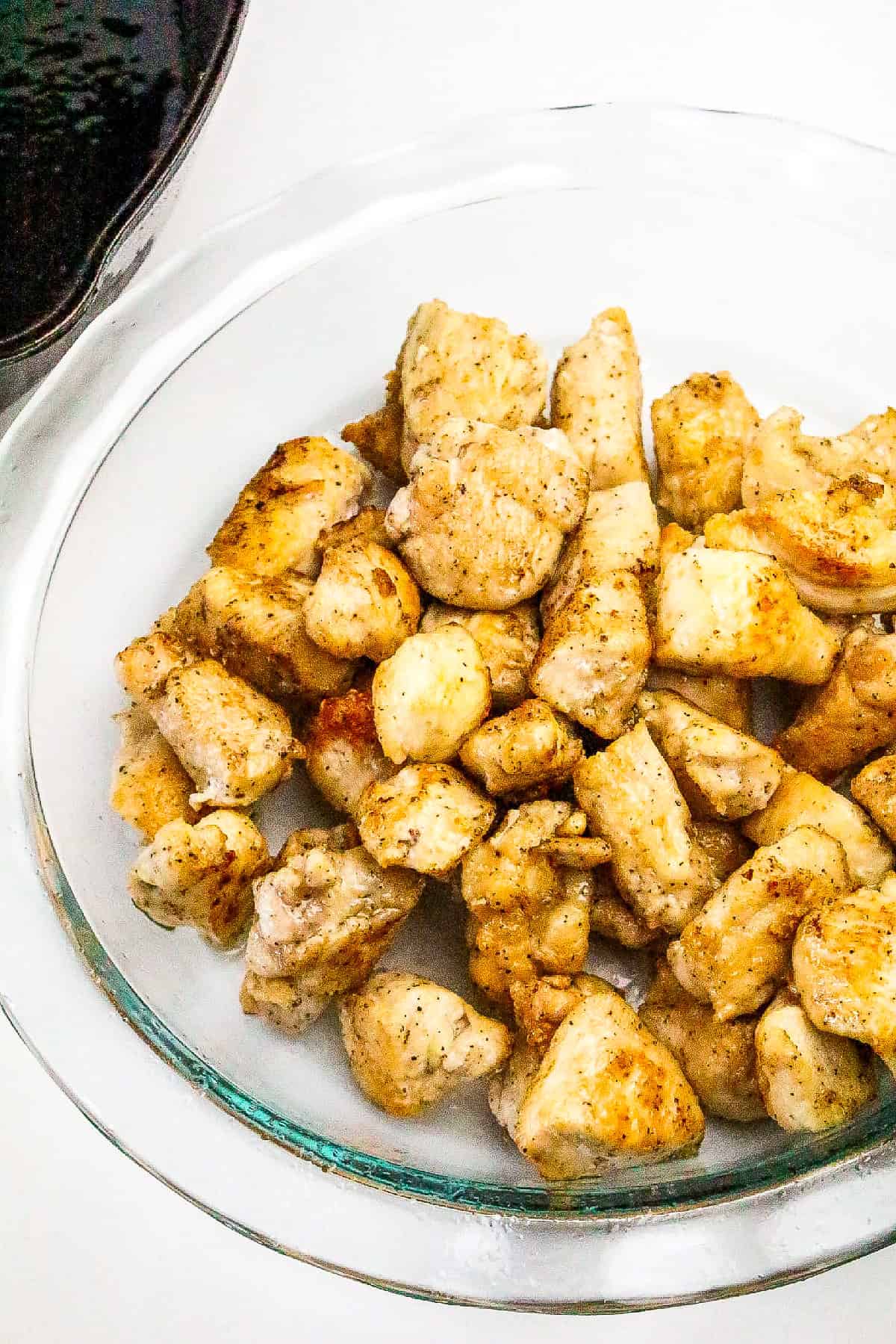 Golden brown fried chicken chunks resting on a glass plate after pan frying.