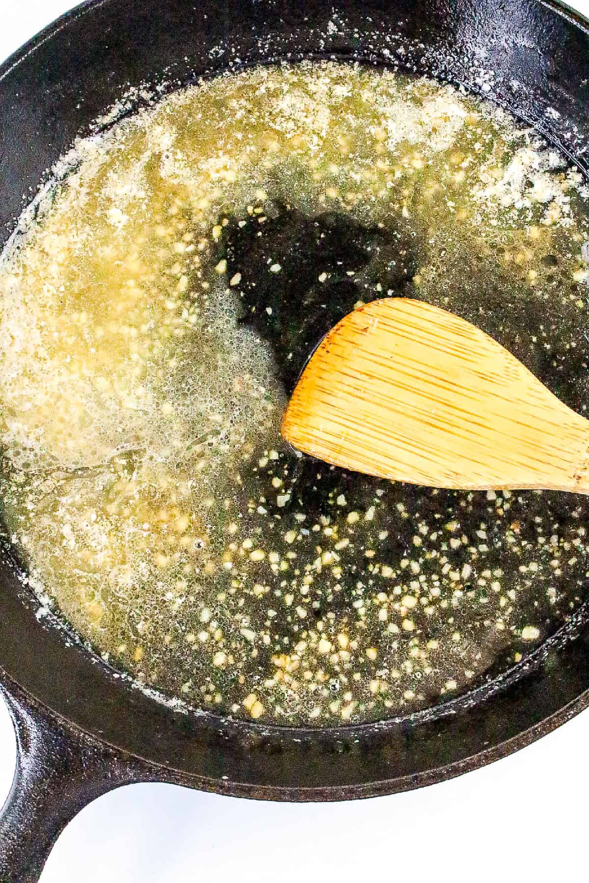 Garlic honey butter sauce simmering in a cast iron pan, being stirred with a wooden spatula.