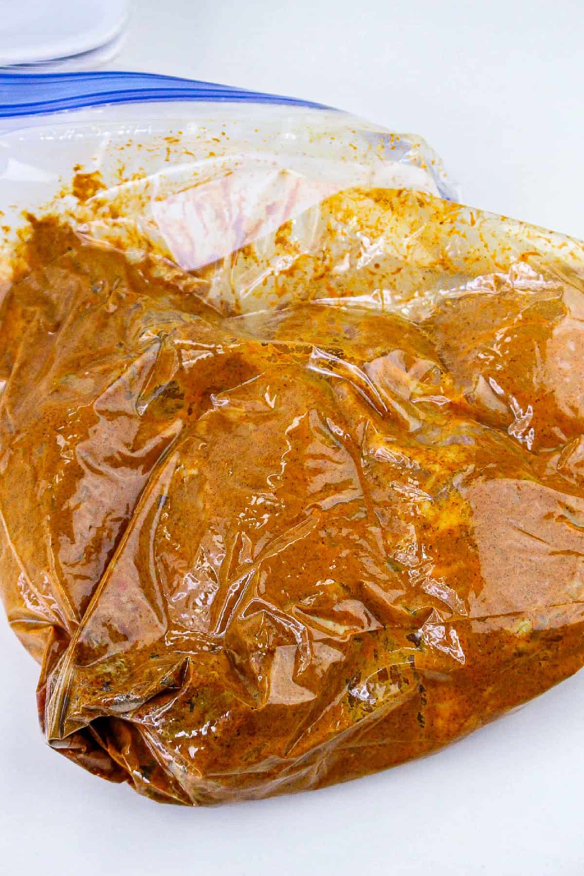 Chicken coated in spiced yogurt marinade inside a resealable bag.