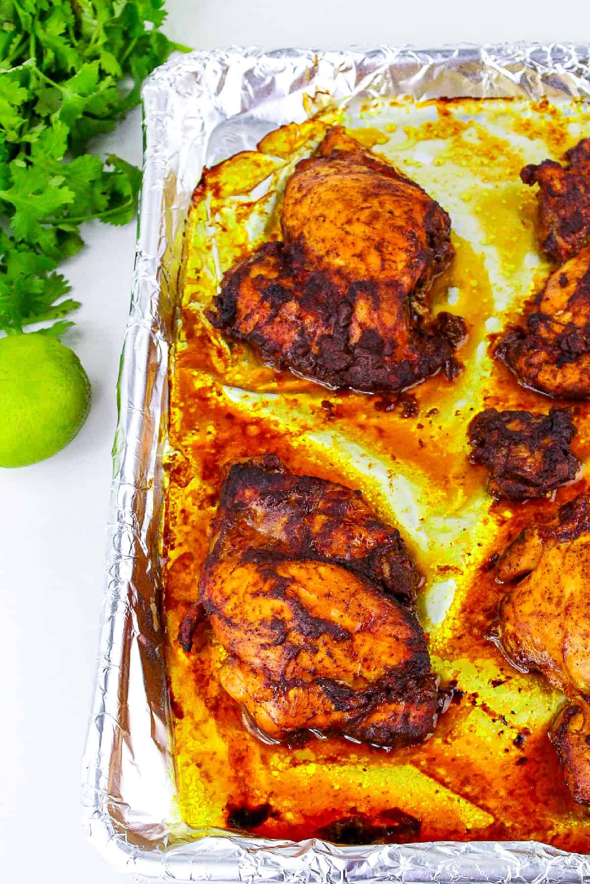 Close-up of baked tandoori masala chicken thighs with crispy edges on foil tray.