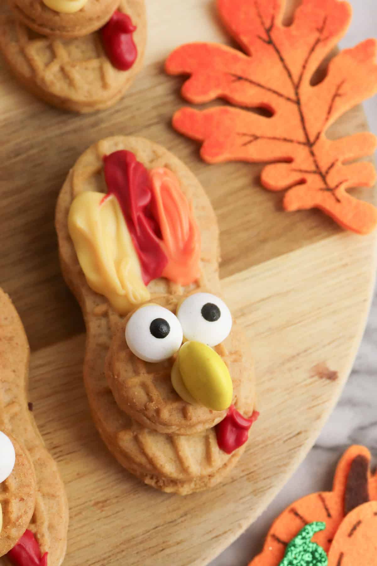 Close-up of a single Nutter Butter turkey cookie with candy eyes, yellow M&M beak, and colorful icing feathers.