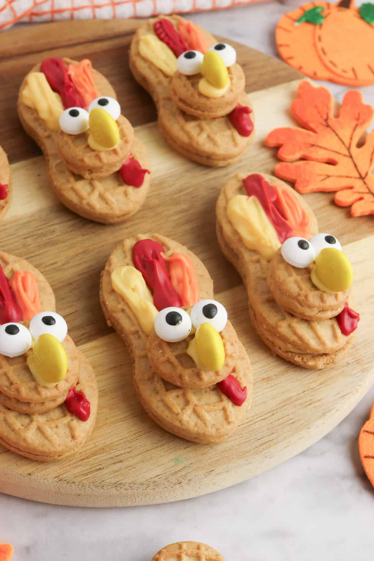 Close-up of Nutter Butter turkey cookies with candy eyes, icing feathers, and M&M beaks displayed on a wooden board.