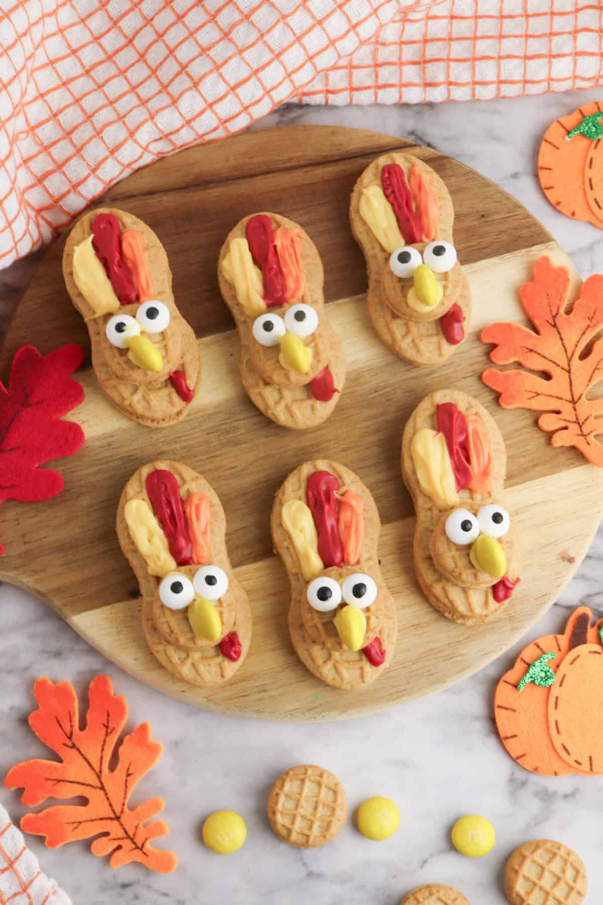 Six Nutter Butter turkey cookies arranged on a wooden serving board with fall leaf decorations and candy pieces.