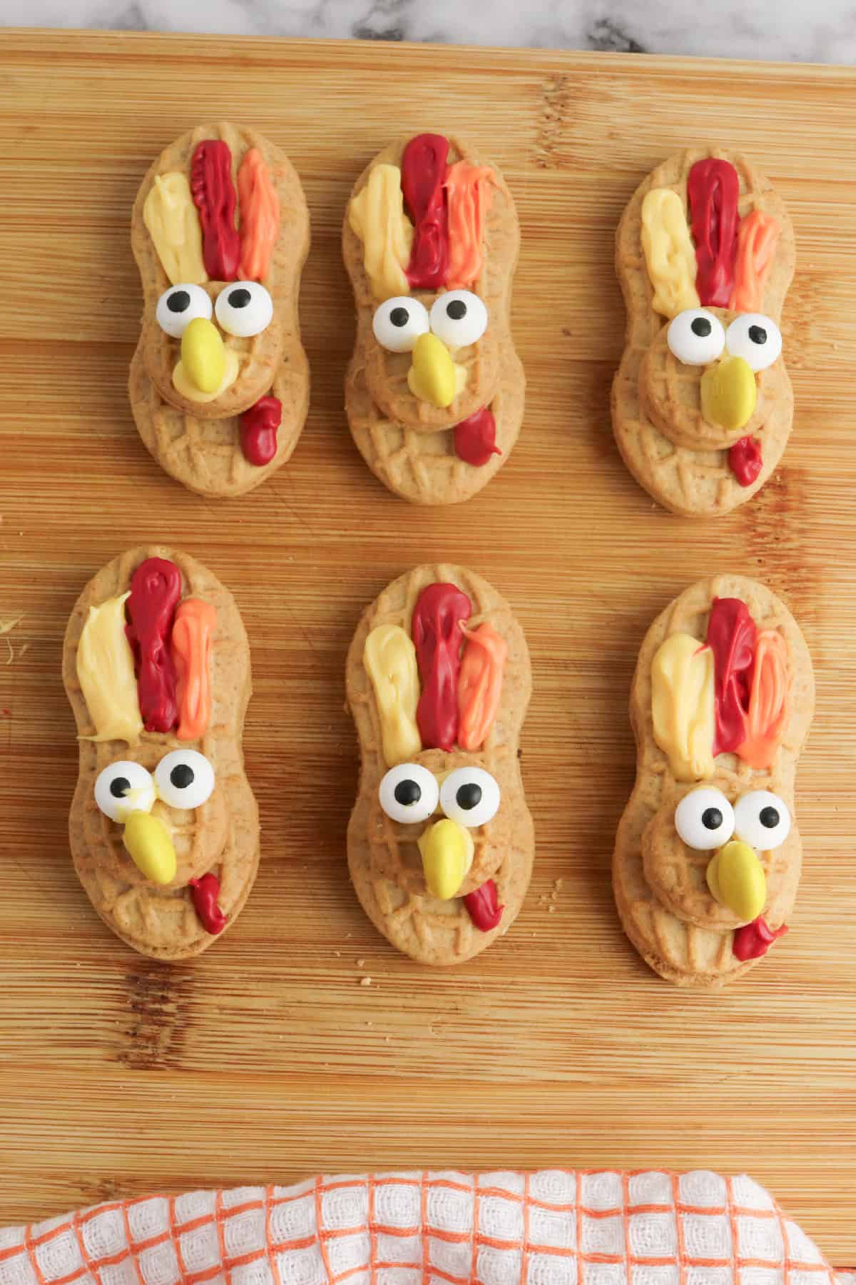 Cute Thanksgiving turkey cookies made with Nutter Butters, candy eyes, colorful icing feathers, and yellow candy beaks.