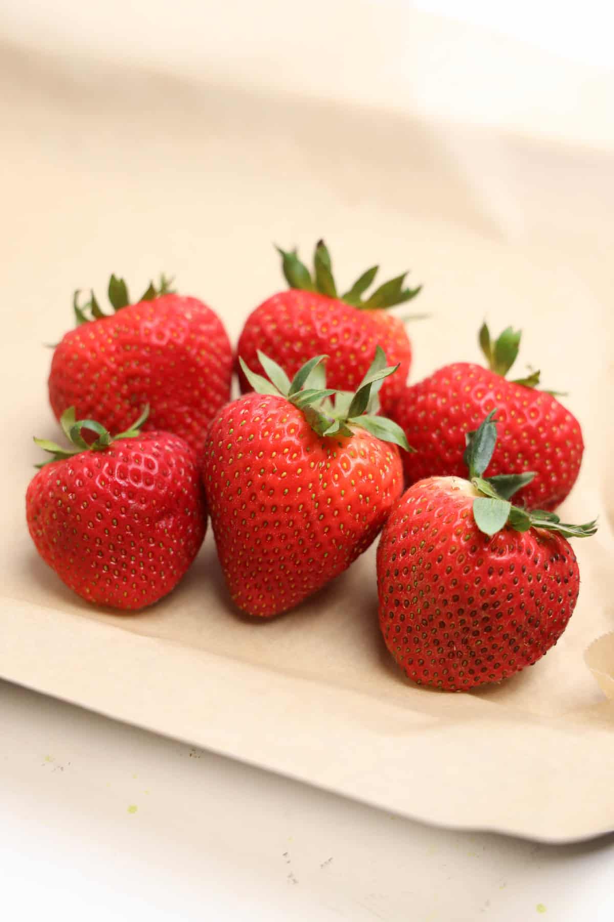 Fresh ripe strawberries arranged on a parchment-lined baking sheet, ready for dipping.