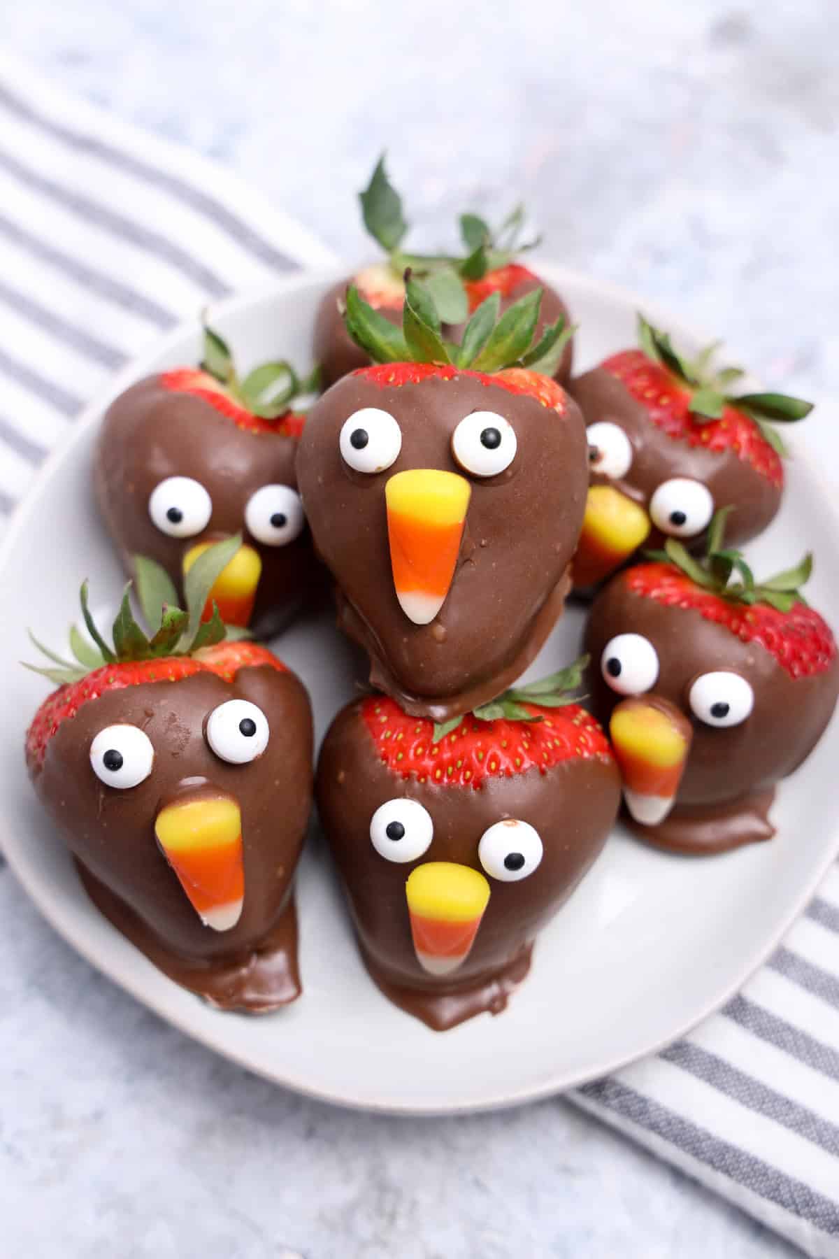 Plate of chocolate-covered strawberry turkeys with candy corn beaks and candy eyes, festive Thanksgiving dessert.