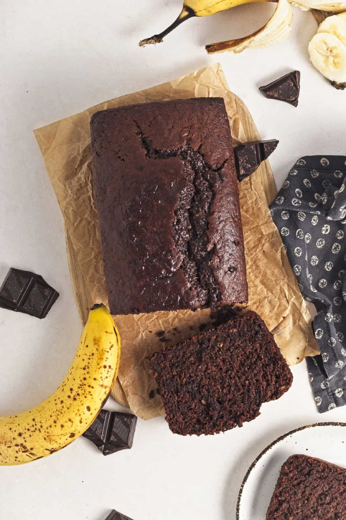 Overhead view of freshly baked vegan chocolate banana bread on parchment with banana and chocolate pieces.