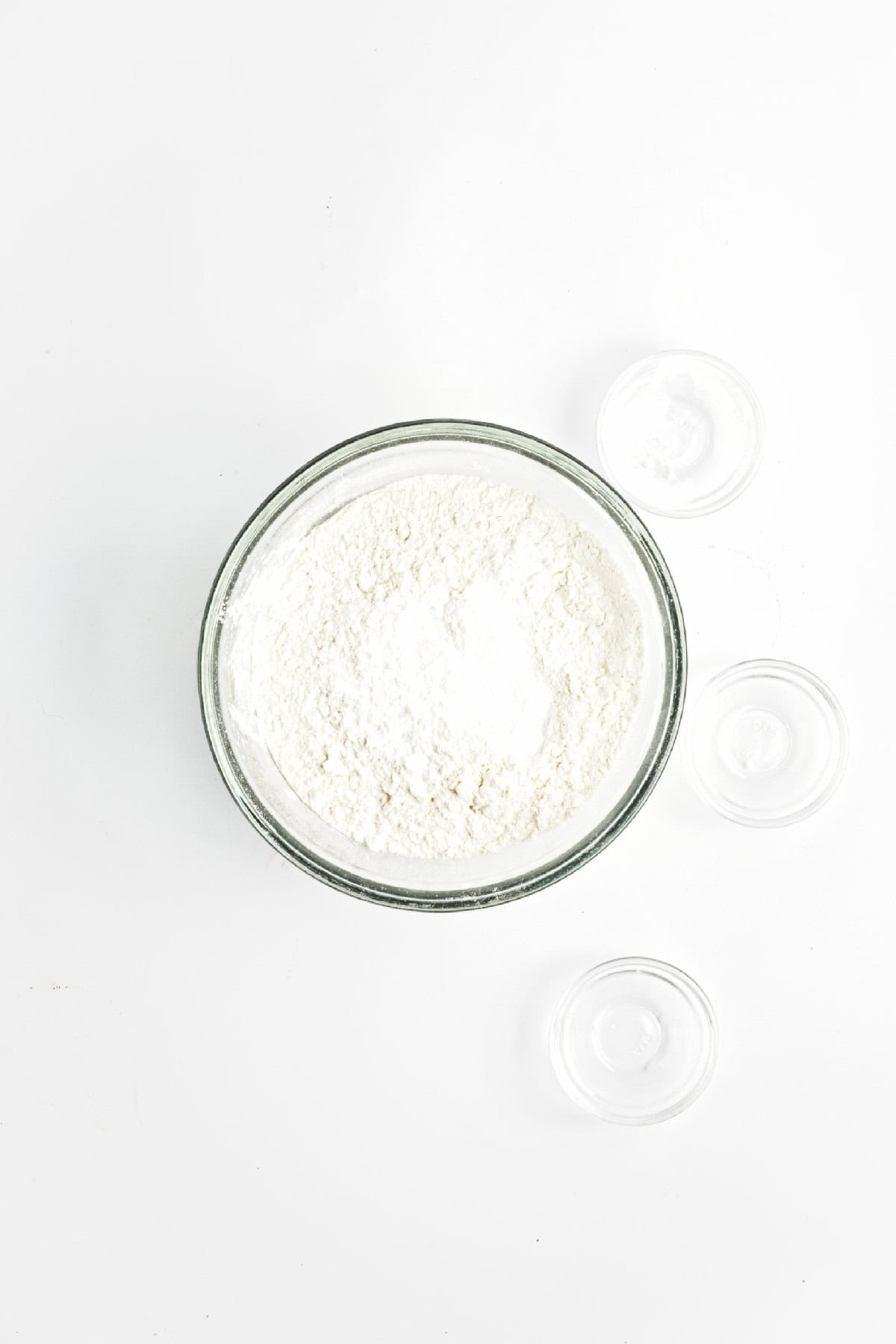 Glass bowl filled with flour and baking ingredients on a white surface – dry ingredients for vegan chocolate banana bread.