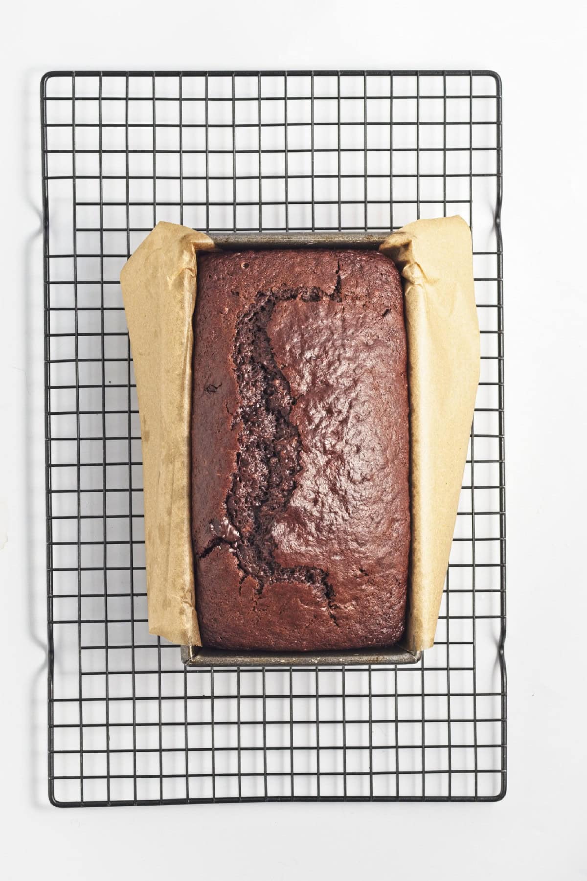Freshly baked vegan chocolate banana bread in loaf pan cooling on wire rack – finished loaf with crackled top.