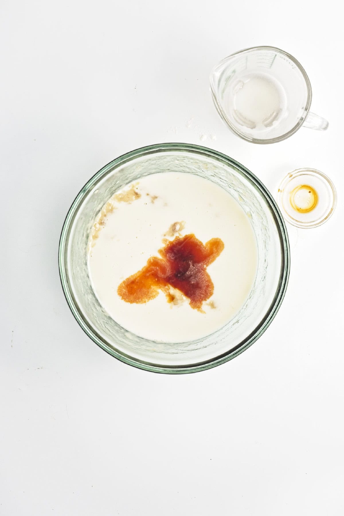 Oat milk and vanilla added to mashed bananas in a glass bowl – wet ingredients for vegan chocolate banana bread.