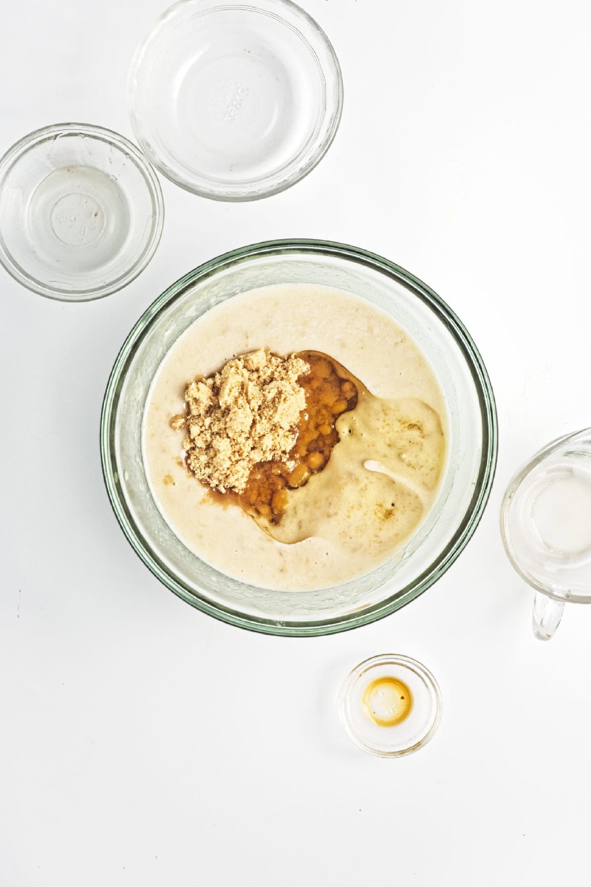 Brown sugar poured into wet banana mixture in a glass bowl – mixing sweetener for vegan chocolate banana bread.