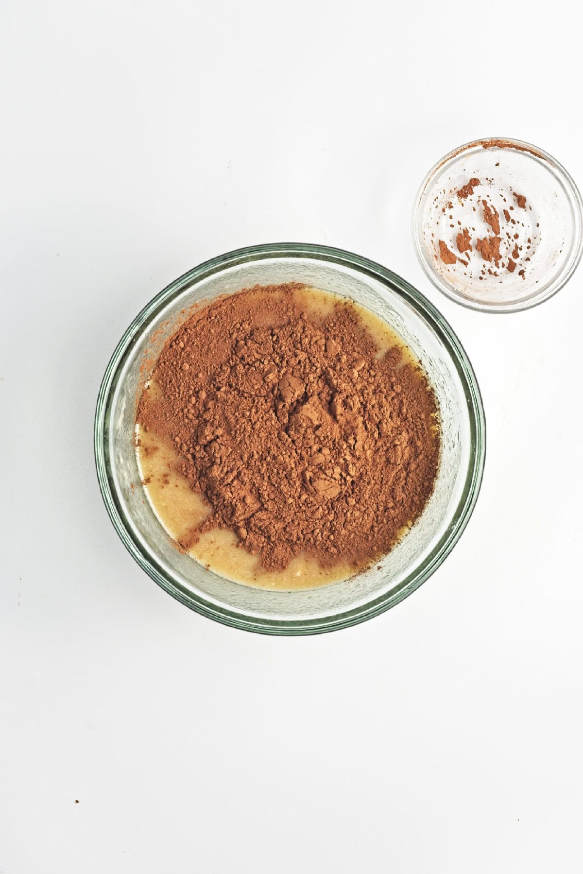 Cocoa powder added on top of banana mixture in a glass bowl – chocolate flavor for vegan banana bread batter.