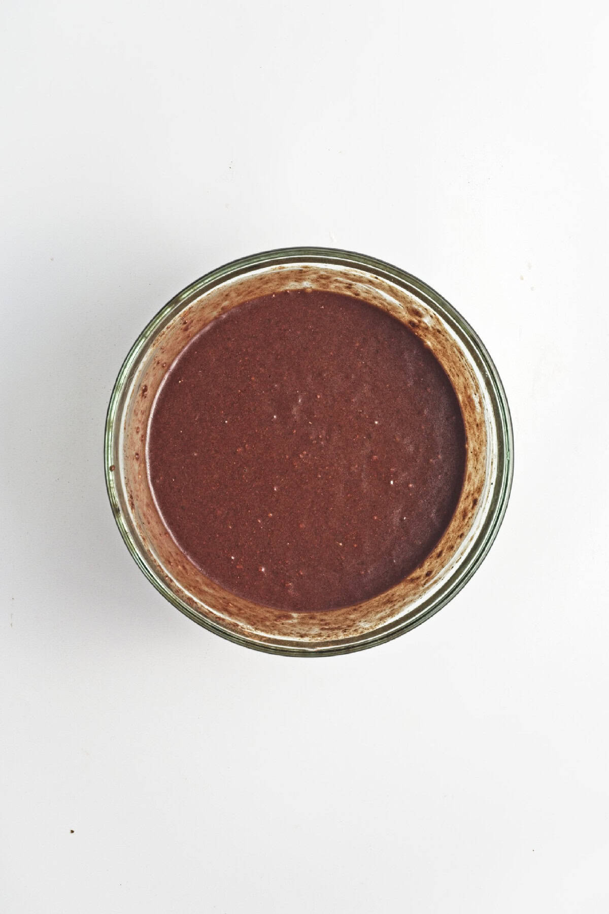 Cocoa powder added on top of banana mixture in a glass bowl – chocolate flavor for vegan banana bread batter.
