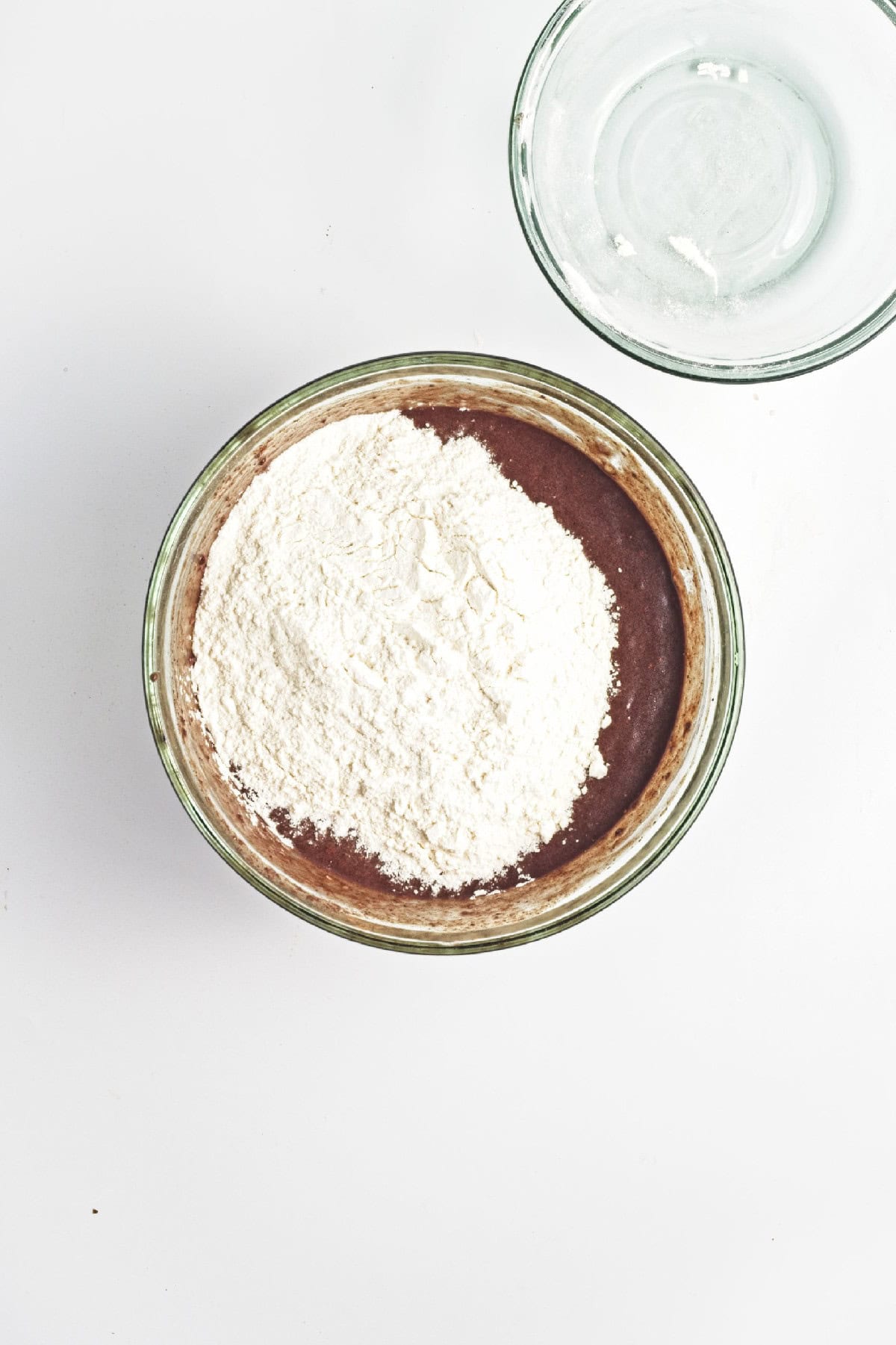 Flour folded into chocolate banana batter in a glass bowl – combining dry and wet ingredients for vegan banana bread.