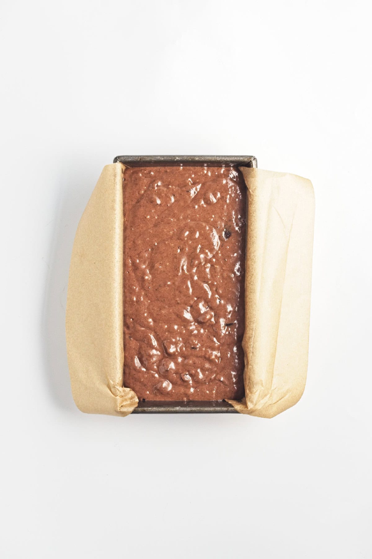 Chocolate banana bread batter poured into a parchment-lined loaf pan – ready to bake.