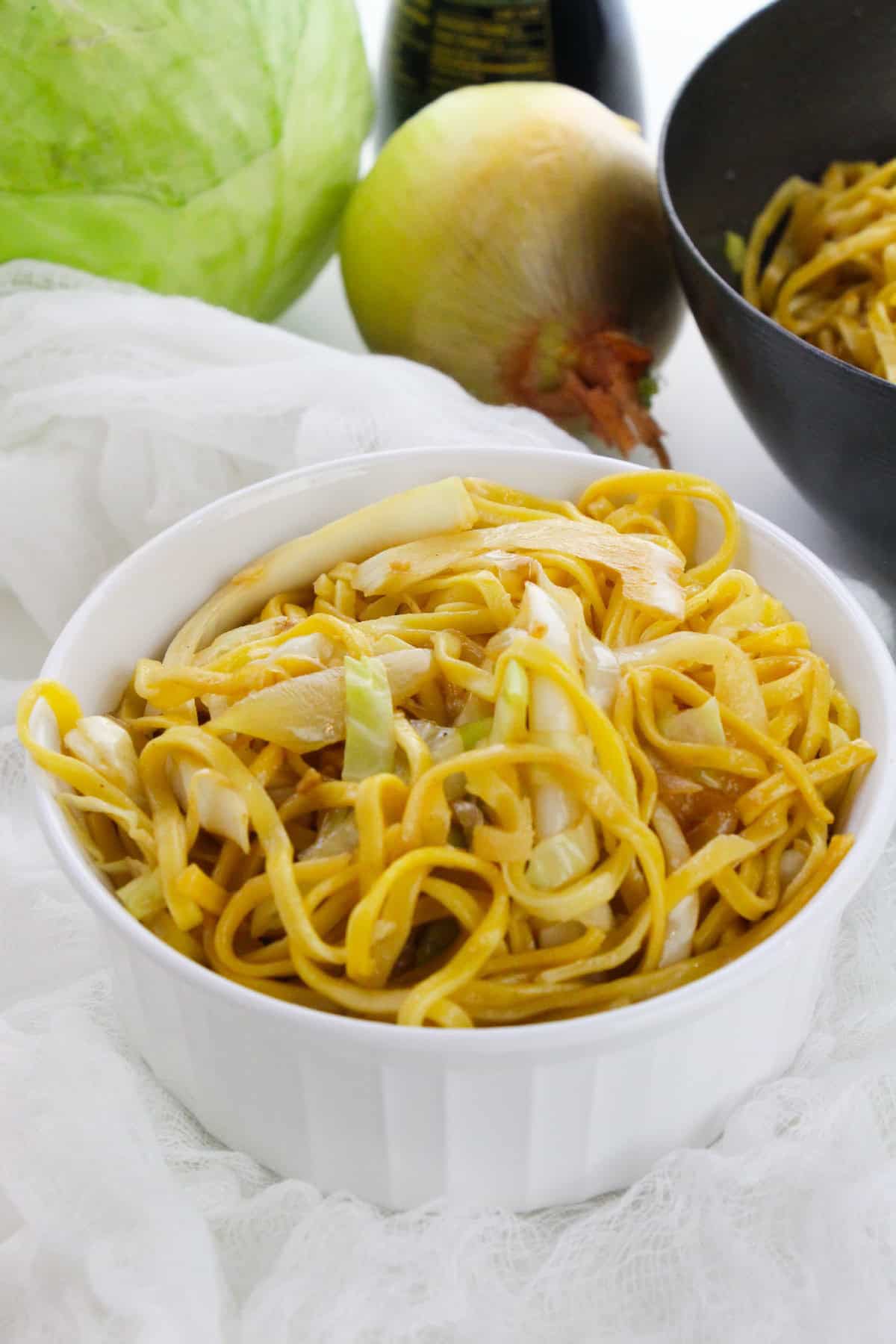 Healthy cabbage chow mein with onions and noodles in a white serving bowl.