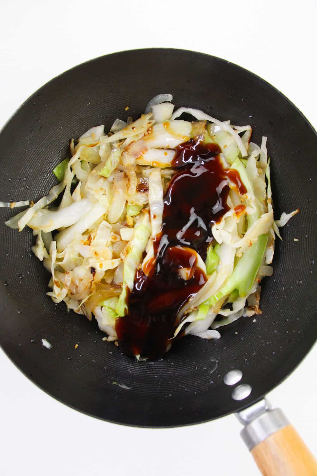 Stir-fried cabbage in wok topped with soy sauce and oyster sauce.