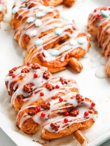 Festive cinnamon roll Christmas tree pastries decorated with icing and colorful sprinkles on a baking tray, holiday dessert idea.