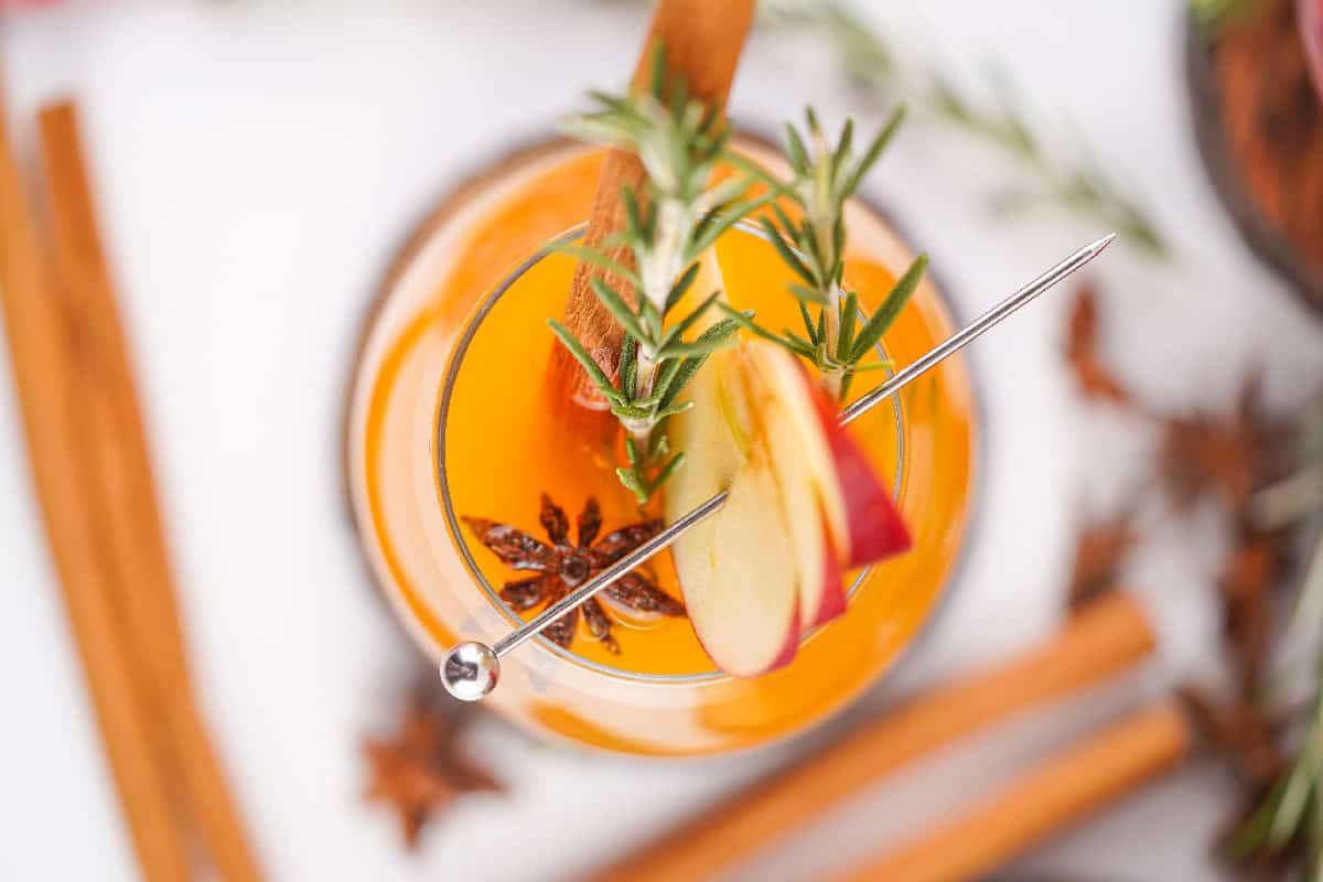 Overhead view of a glass of Fireball apple cider garnished with apple slices, rosemary, star anise, and a cinnamon stick.