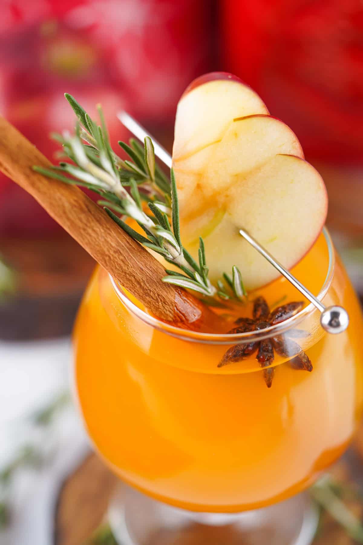 Close-up of a Fireball apple cider cocktail with apple slices, rosemary, and cinnamon, highlighting the garnish and vibrant orange color.