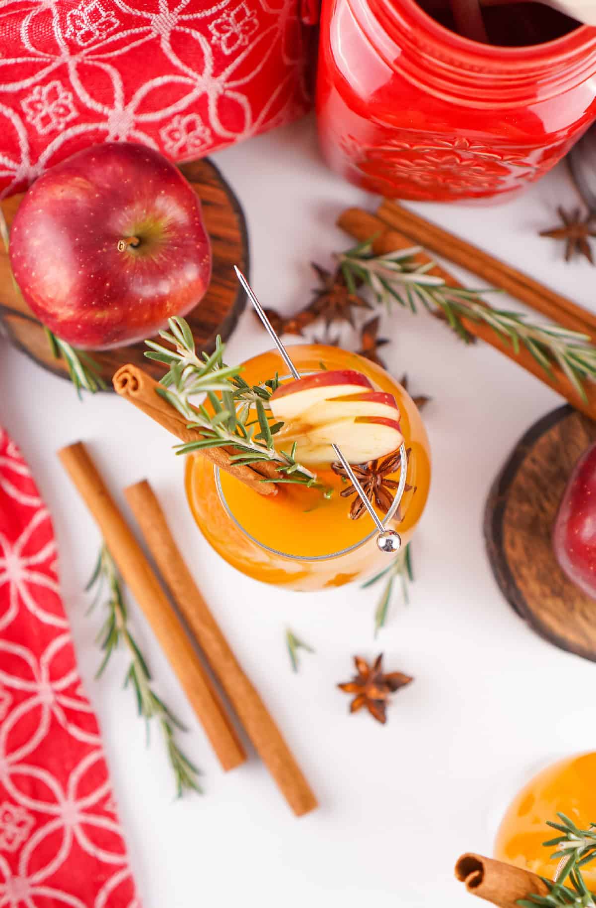Overhead shot of Fireball apple cider cocktails garnished with apple slices, rosemary, and cinnamon, surrounded by apples, cinnamon sticks, and festive decor.