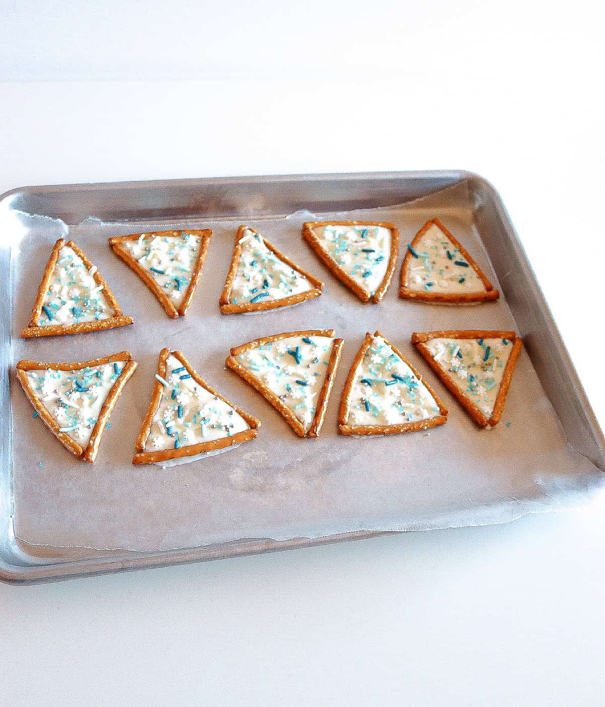 Tray of pretzel triangles filled with white chocolate and topped with blue and white sprinkles.
