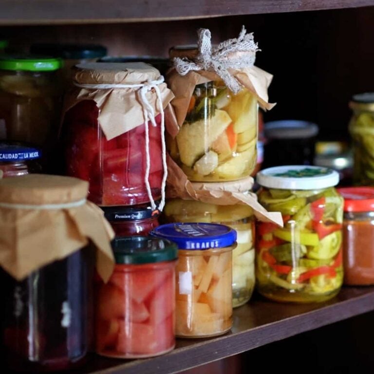 Pickled vegetables in glass jars on a kitchen shelf.