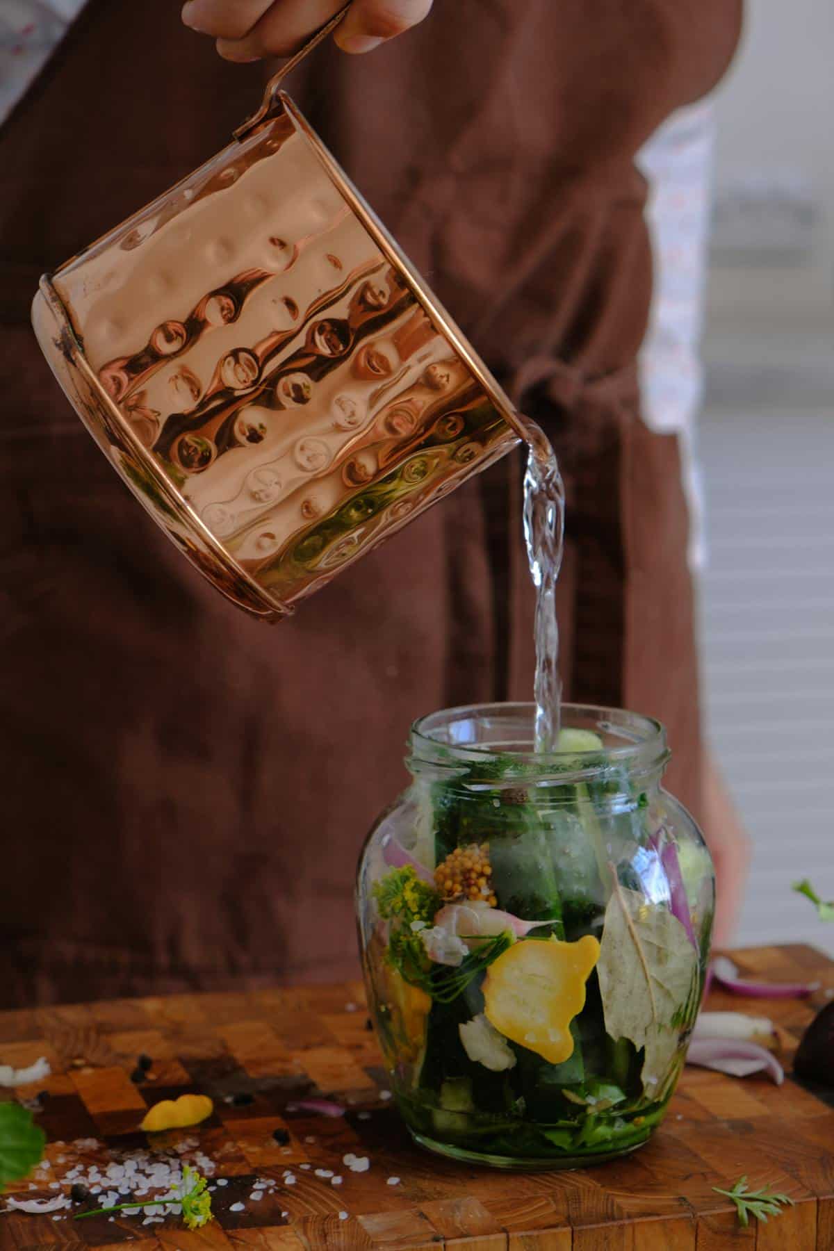Shiny copper mug with water being poured into a jar filled with fresh vegetables and herbs.