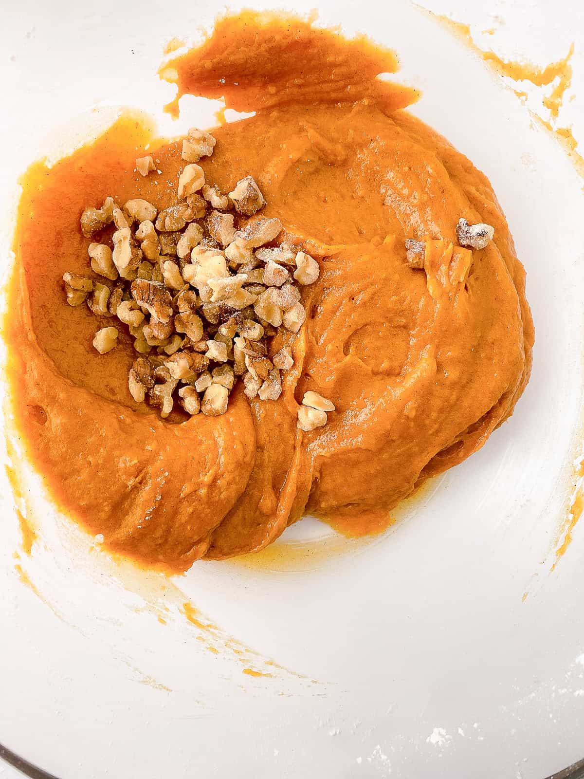 Pumpkin bread batter in a mixing bowl topped with chopped walnuts before folding together.