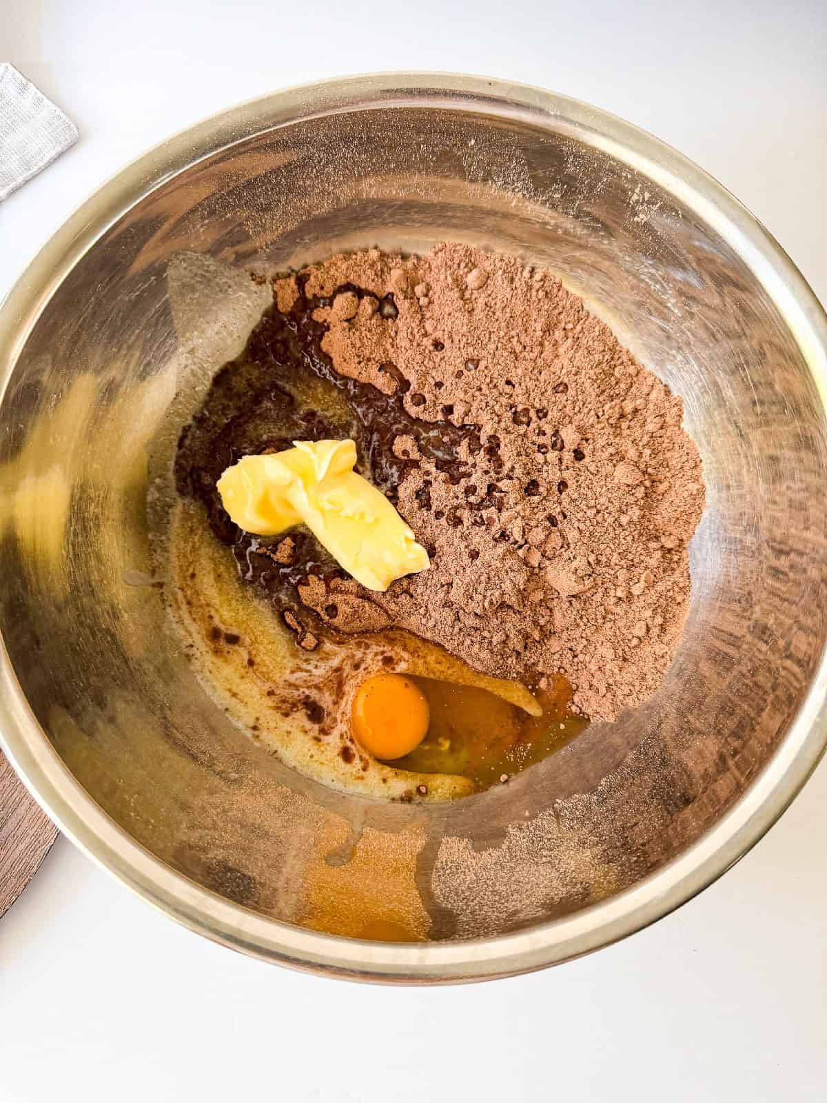 Mixing bowl with cocoa powder, butter, sugar, and an egg ready to be blended for brownie batter.