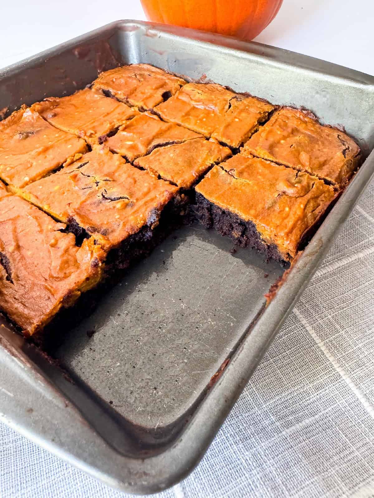 Pumpkin brownies with one piece removed from the pan showing the fudgy chocolate brownie layer inside.