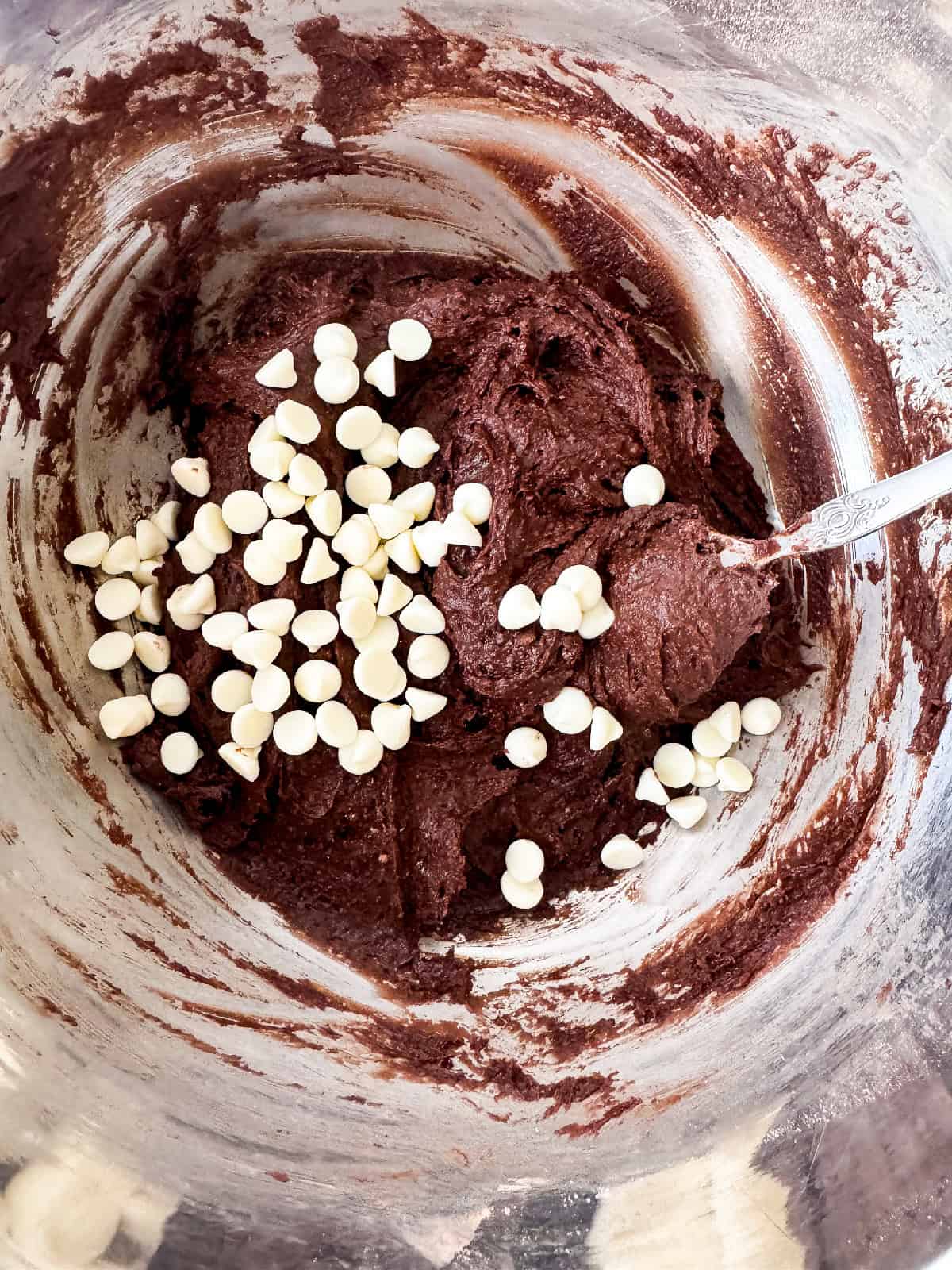 Chocolate brownie batter in a bowl with white chocolate chips sprinkled on top before stirring.