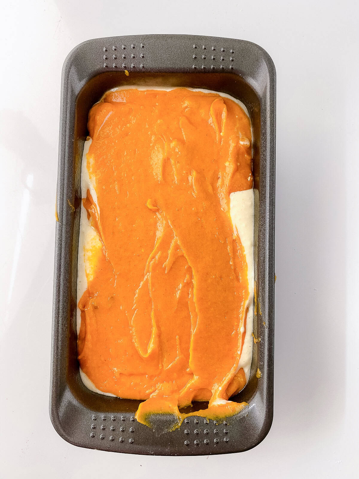Loaf pan filled with alternating layers of pumpkin batter and cream cheese mixture, ready to bake.