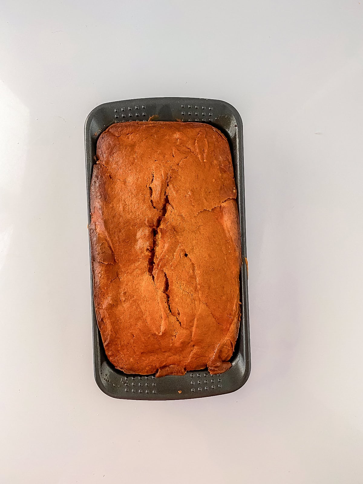 Freshly baked cream cheese pumpkin bread cooling in the loaf pan with a golden-brown top.