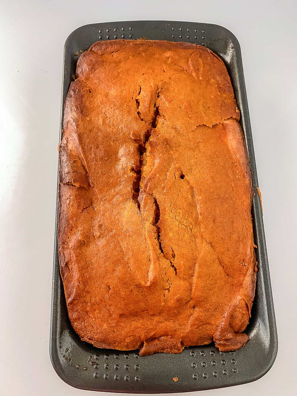 Close-up of baked cream cheese pumpkin bread in the pan showing a cracked, golden crust.