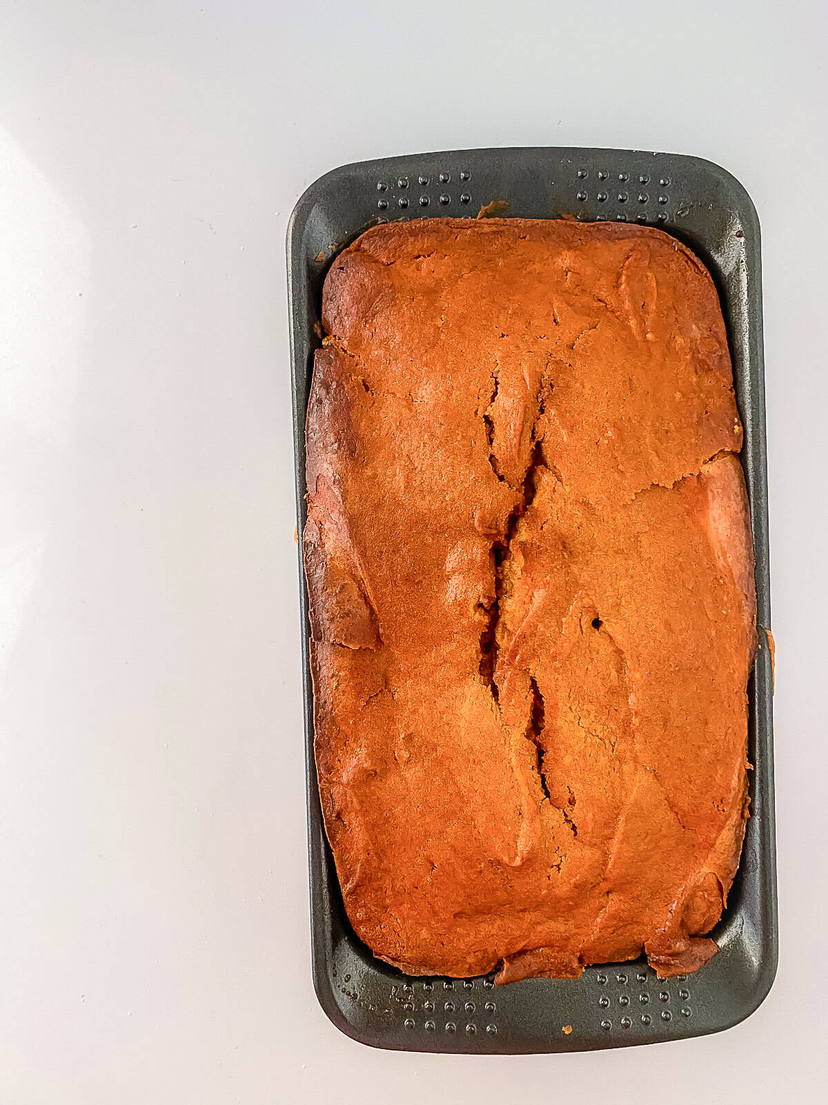 Baked cream cheese pumpkin bread in the loaf pan on a white surface, ready to slice.