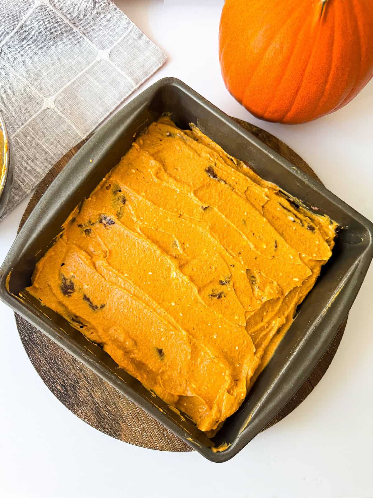 Unbaked pumpkin brownie mixture evenly spread in a square baking pan before going into the oven.