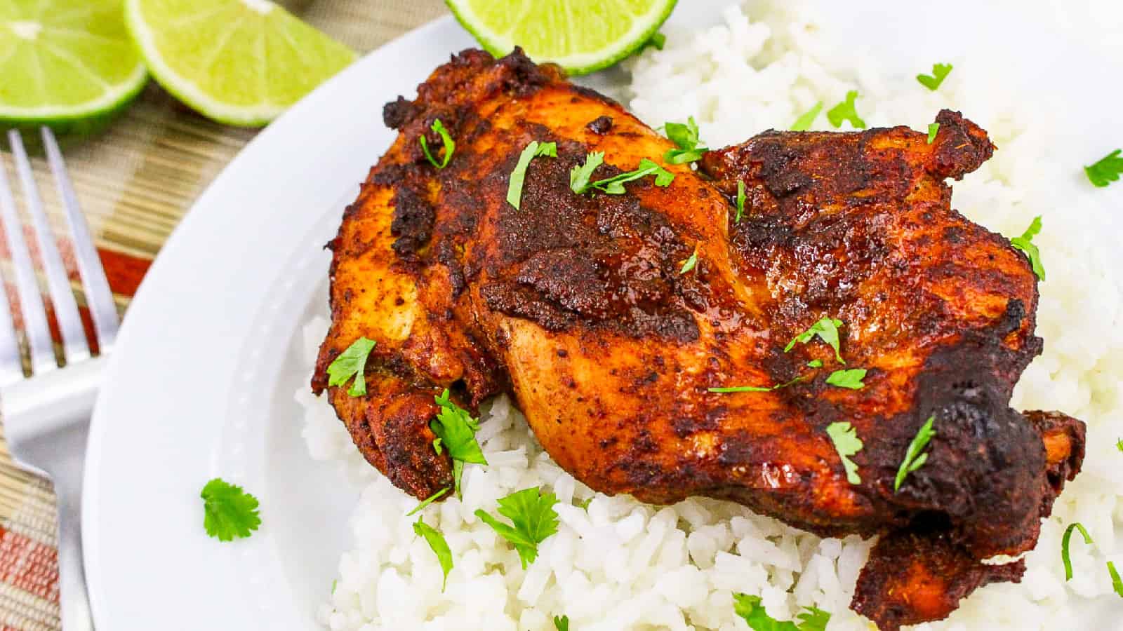 Close-up view of spiced tandoori masala chicken thigh on white rice with green cilantro leaves.
