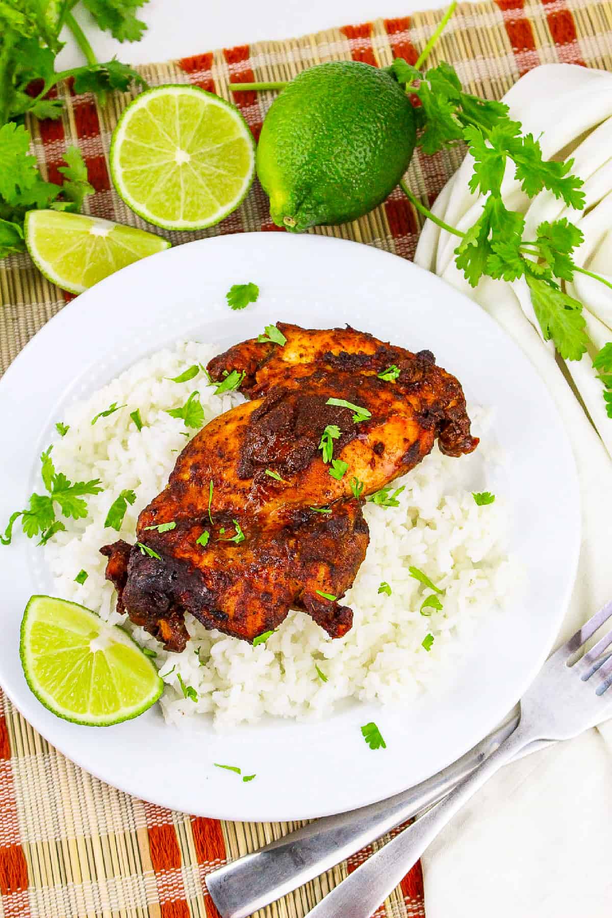 Tandoori masala chicken served over fluffy white rice with lime wedges and fresh cilantro on a white plate.