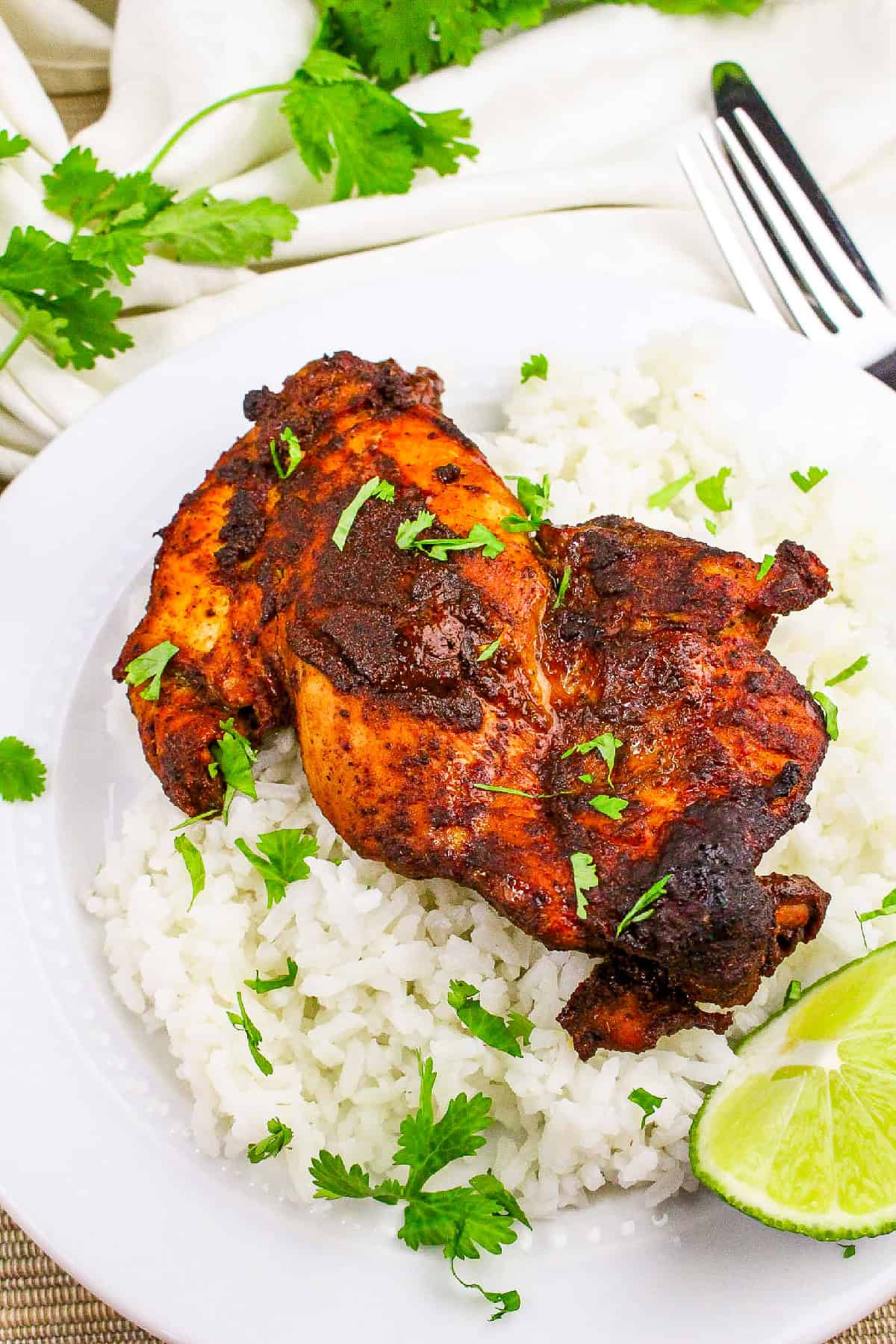 Juicy baked tandoori masala chicken on steamed rice with cilantro and lime on a white dinner plate.
