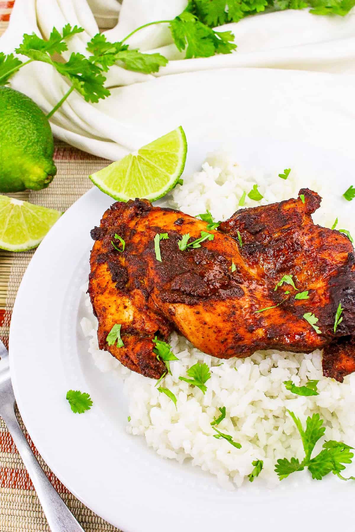 Juicy baked tandoori masala chicken on steamed rice with cilantro and lime on a white dinner plate.